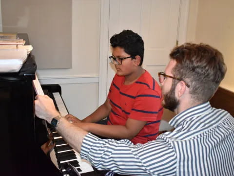 a person playing a piano with another man watching