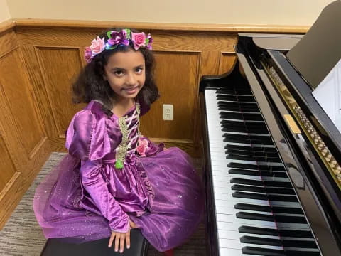 a girl in a purple dress sitting next to a piano