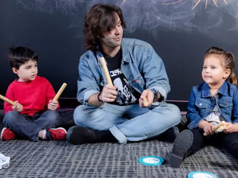 a person and two kids sitting on the floor with sticks in their hands