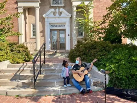 a person playing guitar next to a little girl on stairs