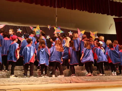 a group of children in blue and red graduation gowns standing on a stage