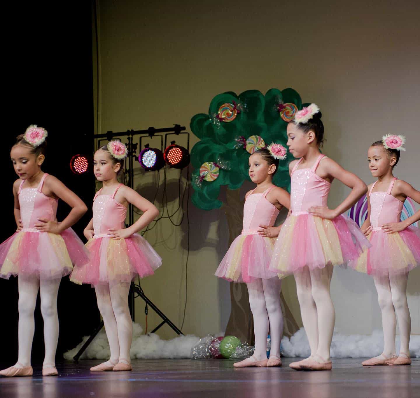 a group of girls in dresses and a green puppet on a stage