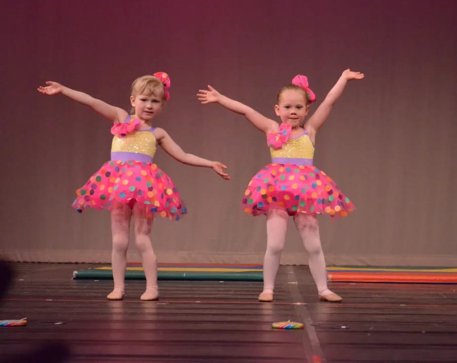 two girls wearing dresses and dancing on a stage