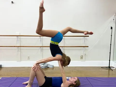 a woman doing a handstand on a mat with another woman lying on her back
