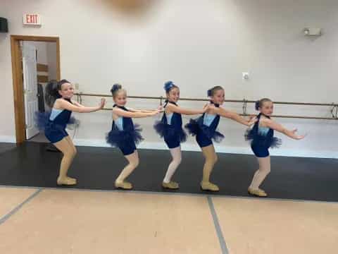 a group of girls in blue uniforms dancing on a wood floor