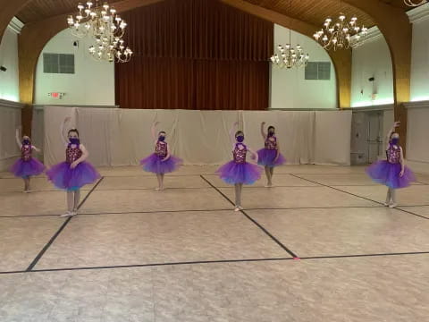 a group of girls in blue and purple dresses dancing in a room