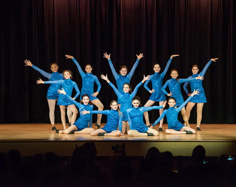 a group of girls in blue dress dancing on a stage