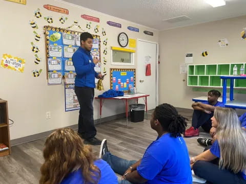 a person standing in front of a group of people sitting in a classroom