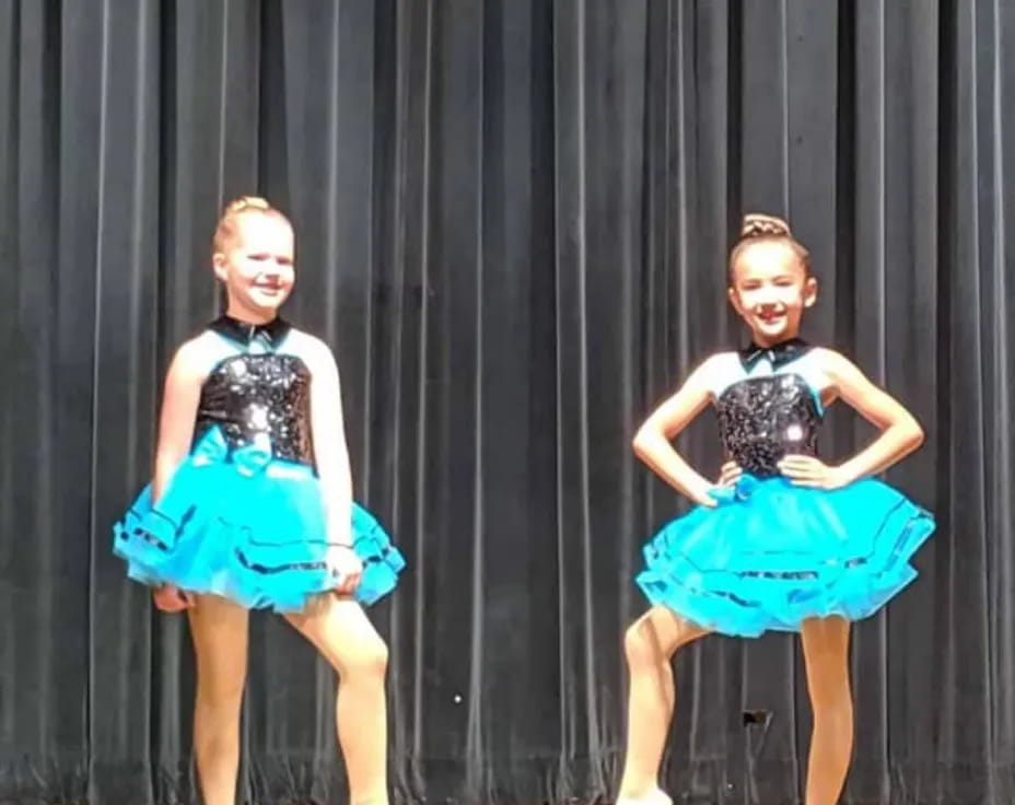 a couple of girls wearing dresses and dancing on a stage