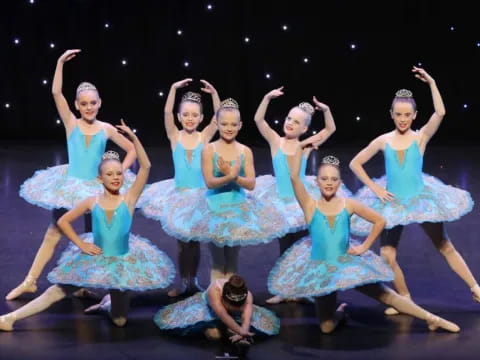 a group of girls in blue dresses dancing on a stage with Marriott Theatre in the background