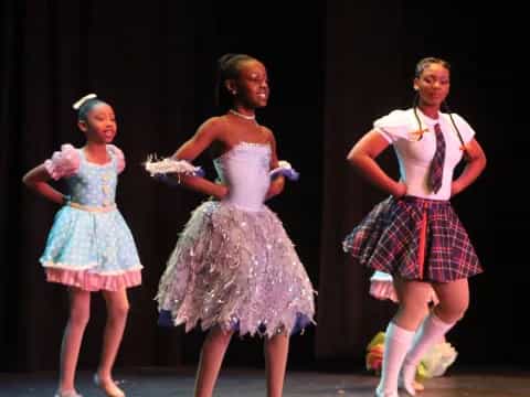 a group of girls wearing dresses and dancing on a stage