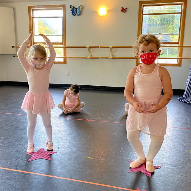 a group of girls wearing pink and white dresses and standing on a mat