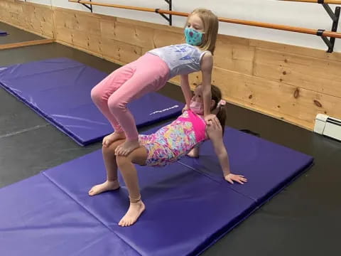 a woman in a pink outfit on a mat with a girl in a blue dress