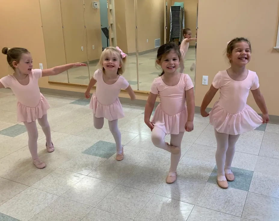 a group of girls wearing pink dresses and dancing in a room