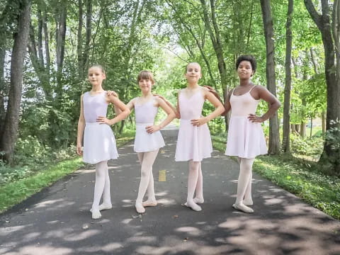 a group of girls in white dresses walking down a path in the woods