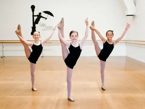 a group of girls in black ballet outfits on a wooden floor