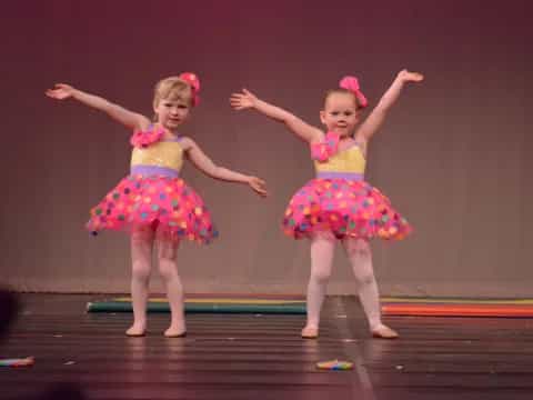 two girls wearing dresses and dancing on a stage