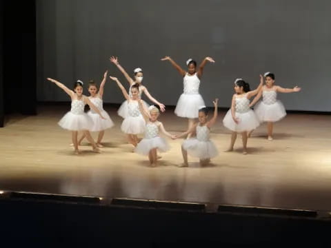 a group of girls in white dresses dancing on a stage