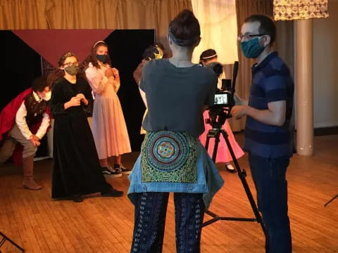 a group of people wearing masks and standing in a room with a wood floor and a curtain