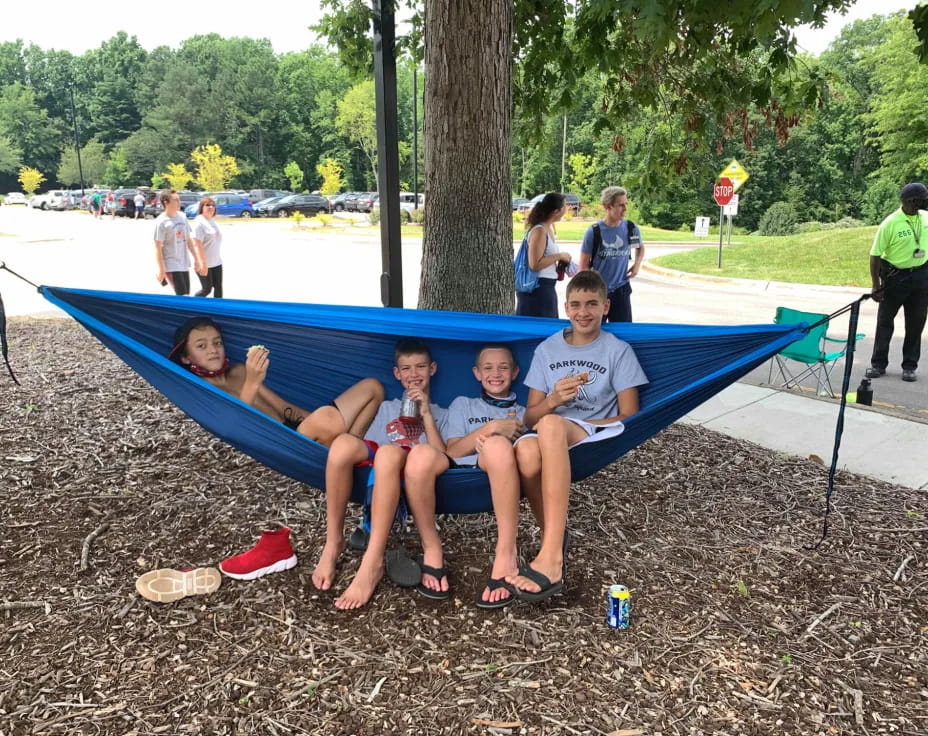 a group of people sitting on a blue trampoline by a tree