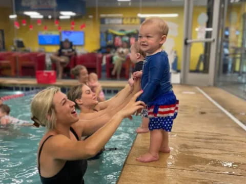 a person holding a baby in a pool with other people in the background