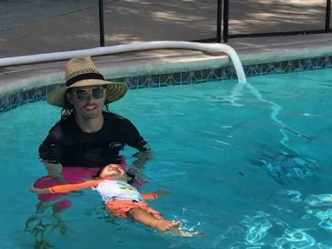 a person in a hat and sunglasses in a pool with a baby