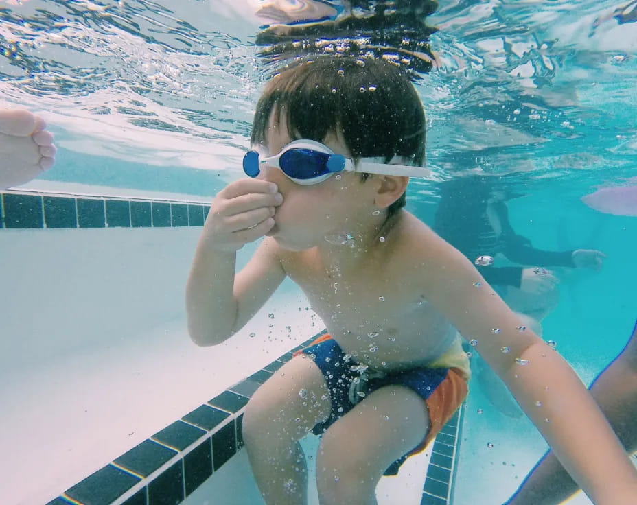 a boy wearing goggles and swimming in a pool