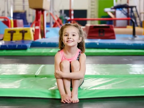a little girl in a swimsuit on a green mat in a gym