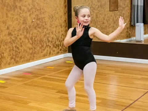 a woman in a black leotard dancing on a wood floor