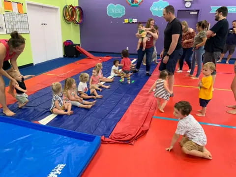 a group of children sitting on a mat in a room with people