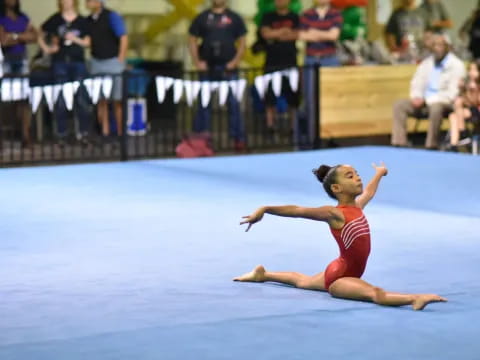 a woman in a leotard dancing on a blue mat in front of a crowd