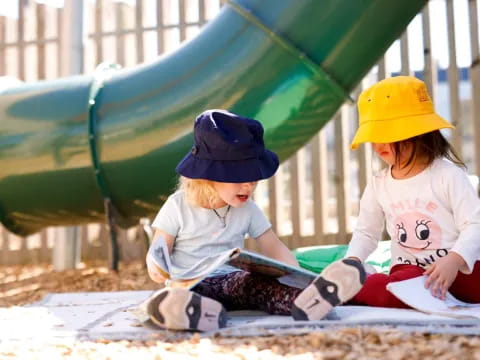 a couple of kids sitting under a green umbrella