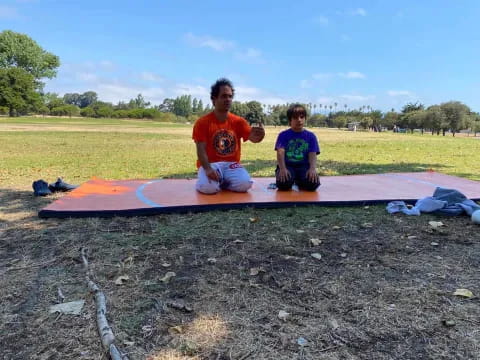 a man and a boy sitting on a mat in a field