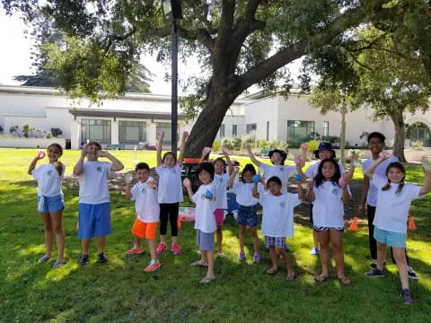 a group of children standing in a line in front of a tree