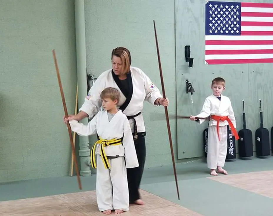 a person and two boys in karate uniforms holding swords