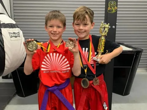 two boys in red and blue uniforms holding trophies