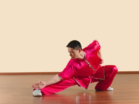 a person in red martial arts uniform squatting on the floor