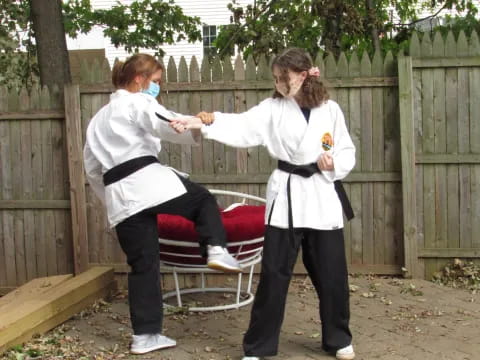 a couple of women in white karate uniforms holding a sword and a white object