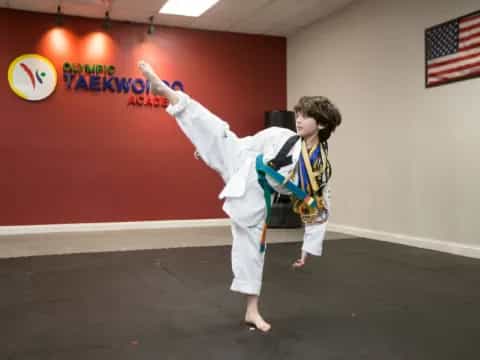 a man in a karate uniform kicking a ball in a room with a flag