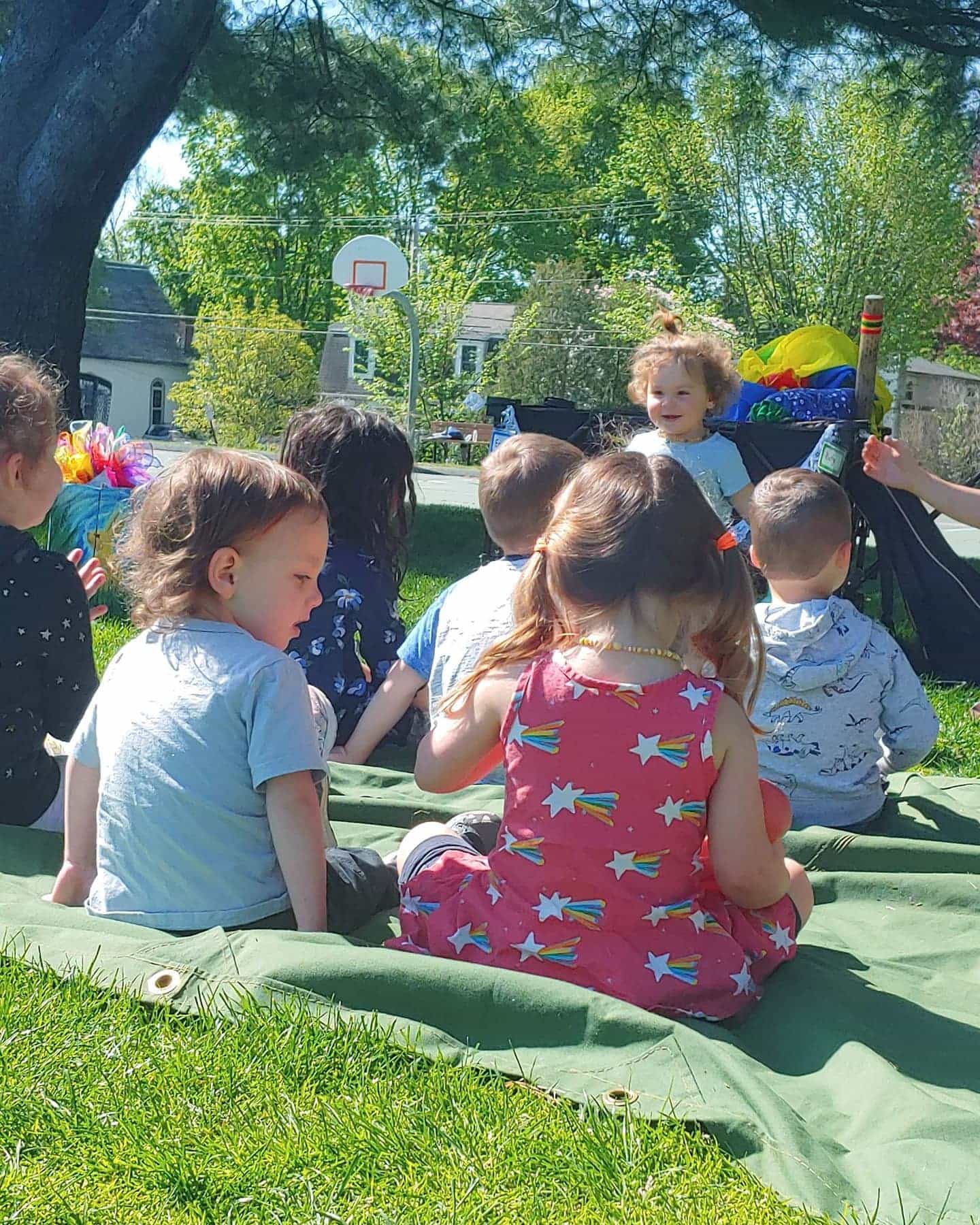 a group of children sitting on a blanket in a grassy area