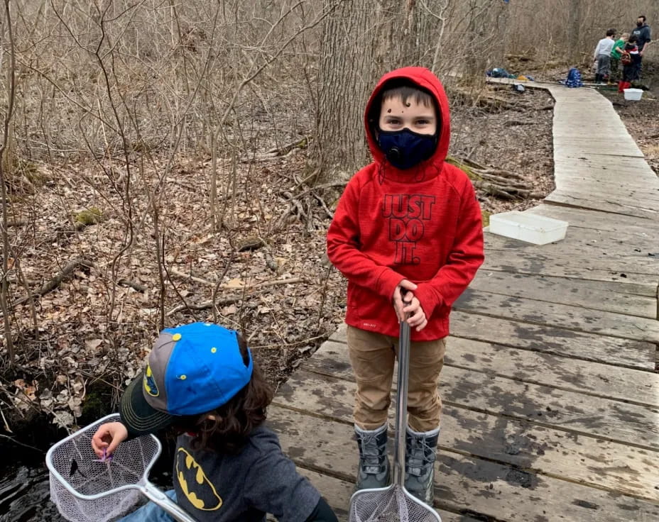 a couple of kids on a wooden bridge with a stick and a bucket