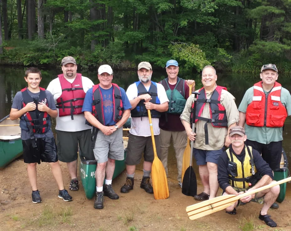 a group of men in life jackets standing in front of a lake