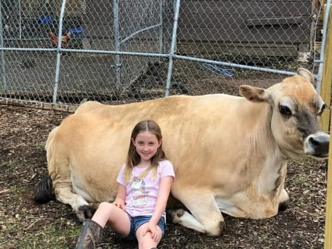 a girl sitting next to a cow