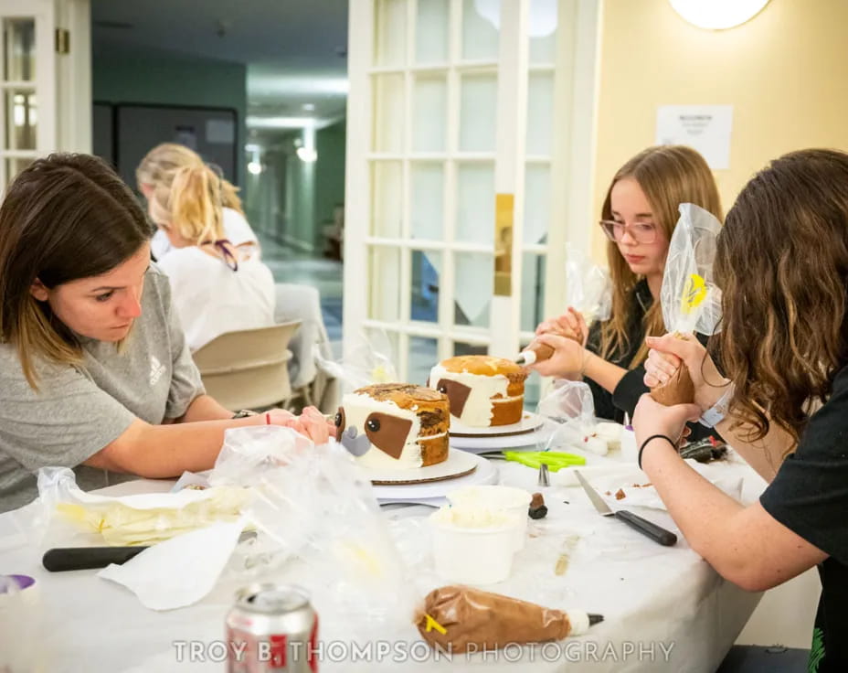 a group of people gather around a table with cakes