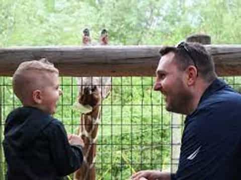 a person and a boy looking at a giraffe through a fence