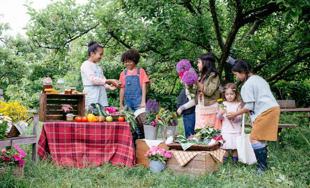 a group of people standing around a table with flowers and fruit