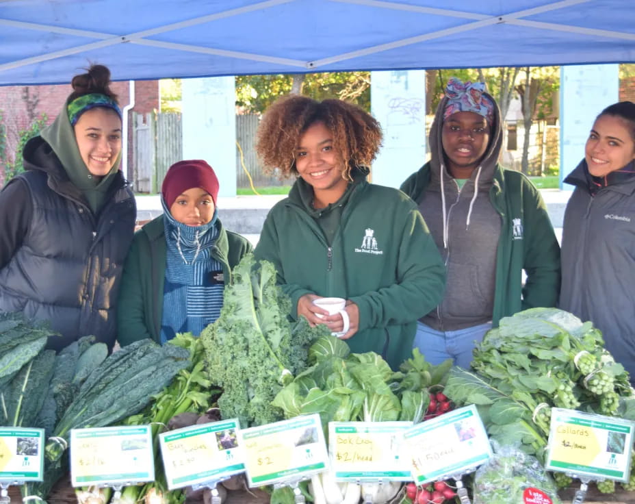 a group of women standing next to some vegetables