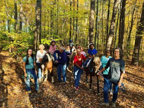 a group of people walking with horses in the woods