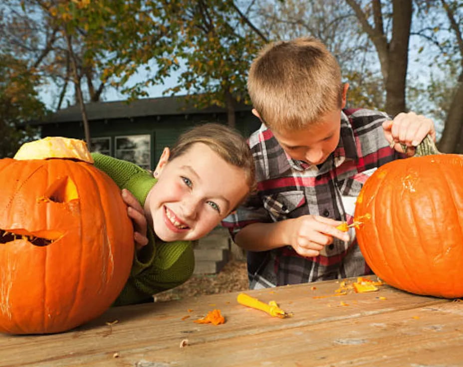 a couple of kids sitting next to a pumpkin and a carved pumpkin