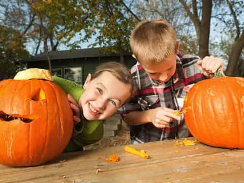 a couple of kids sitting next to a pumpkin and a carved pumpkin